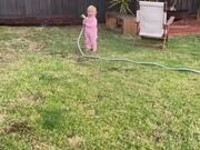 Daughter Sprinkles Water on Dad With Hose