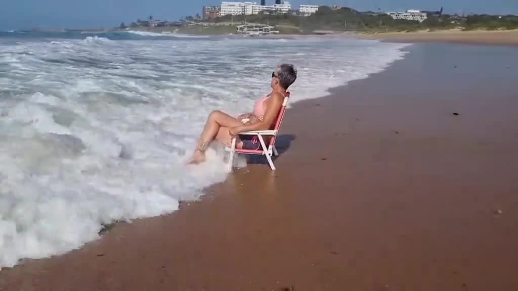 Woman Sitting in Chair Gets Knocked Back by Waves